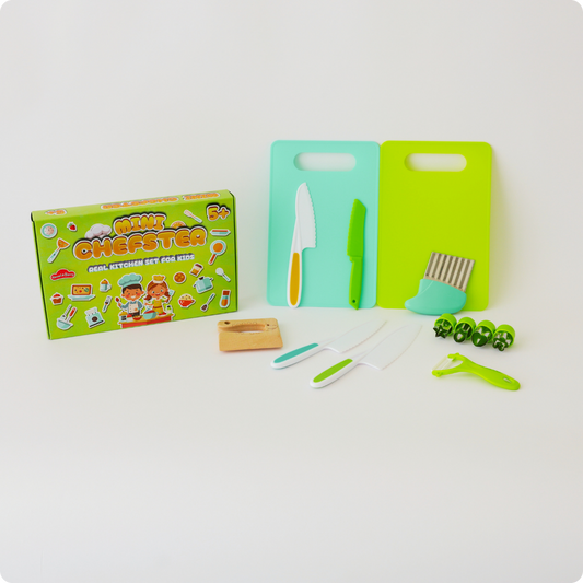 Children's kitchen playset including green cutting board, wooden knife, plastic knife, and other toy kitchen utensils.